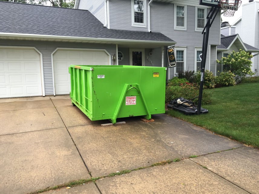 A green dumpster in front of a family home.